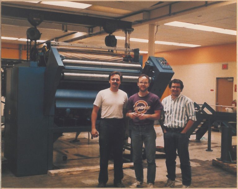Historical photo of men standing by printing machine