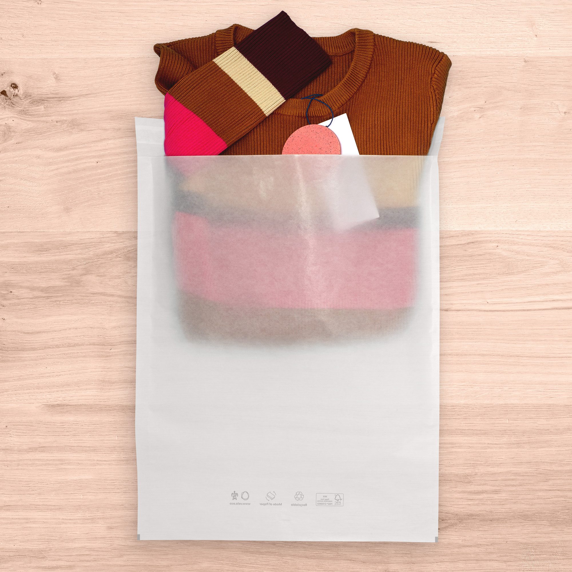 Red and brown sweater being placed into sustainable packaging bag on wood surface